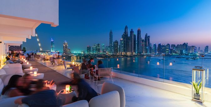 Moderner Außenbereich mit rechteckigem Pool, zwei geflochtenen Stühlen, einer weißen Liege und Blick auf die Stadt Dubai im Hintergrund.