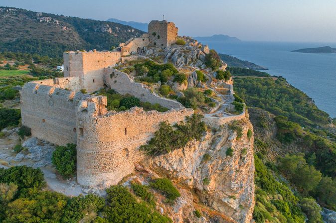 Klostergebäude mit Glockenturm auf einer kleinen Landzunge im Meer mit Spaziergängern und Bäumen