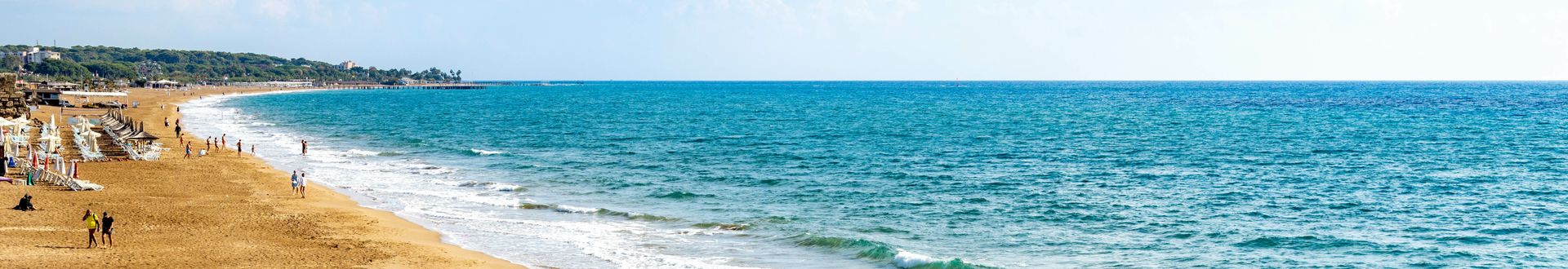 Breiter Sandstrand in Side an der türkischen Riviera mit türkisfarbenem Meer, sanften Wellen und Sonnenliegen entlang der Küste