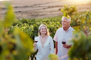 Älteres Paar genießt ein Glas Rotwein bei Sonnenuntergang inmitten eines Weinbergs