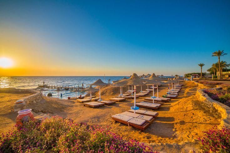 Am Strand von Hurghada stehen Liegen und Sonnenschirme mit Blick auf das Rote Meer, während die Sonne am Horizont untergeht