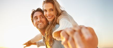 Zwei Personen am Strand; der Mann trägt die Frau auf dem Rücken; Sonnenlicht und sandige Küstenlandschaft im Hintergrund