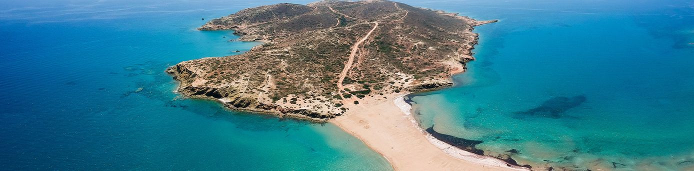 Luftaufnahme einer schmalen Sandzunge, die eine kleine Insel mit dem Festland verbindet, umgeben von türkisfarbenem Meer.