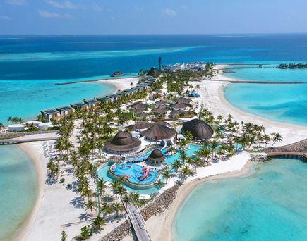 Luftaufnahme des Centara Mirage Lagoon Maldives mit weißem Sandstrand, türkisfarbener Lagune, Palmen und mehreren Poolbereichen