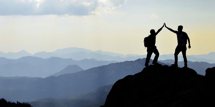 Zwei Bergsteiger geben sich High Five auf Berggipfel bei Sonnenuntergang
