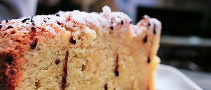 Nahaufnahme eines Stücks hellen Kuchens mit Puderzucker und dunkler Sauce