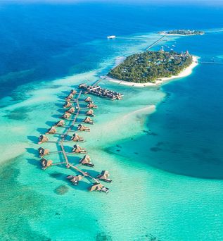Luftaufnahme einer Insel mit Bungalows auf Stelzen, die sich über türkisfarbenes Wasser erstrecken.