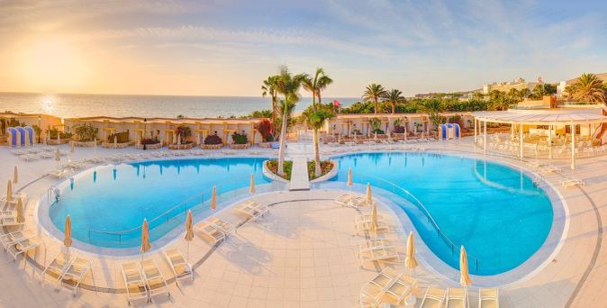 Großer Hotelpool mit Palmen und Liegestühlen am Meer bei Sonnenuntergang