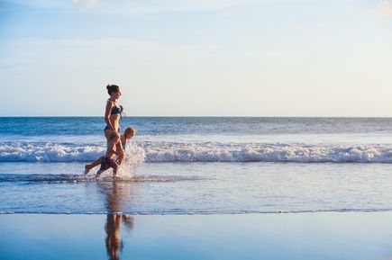 Mutter läuft mit zwei kleinen Kindern am flachen Ufer entlang, während die Wellen ans Ufer rollen