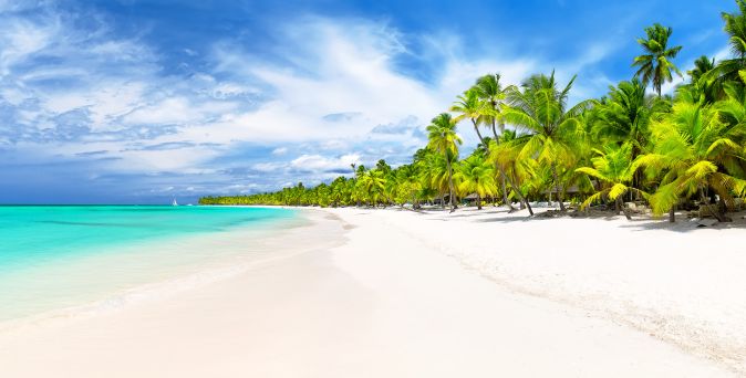 Schwarz-weiß gestreifter Leuchtturm am Sandstrand mit Palmen und klarem blauem Meer unter blauem Himmel