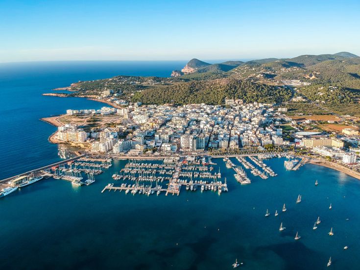 Luftaufnahme von San Antonio Ibiza mit Hafen, Yachten und umliegenden Hügeln unter klarem Himmel