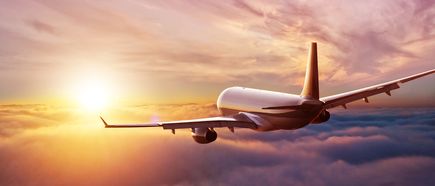 Passagierflugzeug fliegt in Richtung Sonnenuntergang über einer geschlossenen Wolkendecke; stimmungsvolle Himmelsszene im warmen Licht