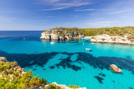 Luftaufnahme der Cala Macarella auf Menorca mit türkisblauem Wasser, Segelbooten und grünen Pinienhängen