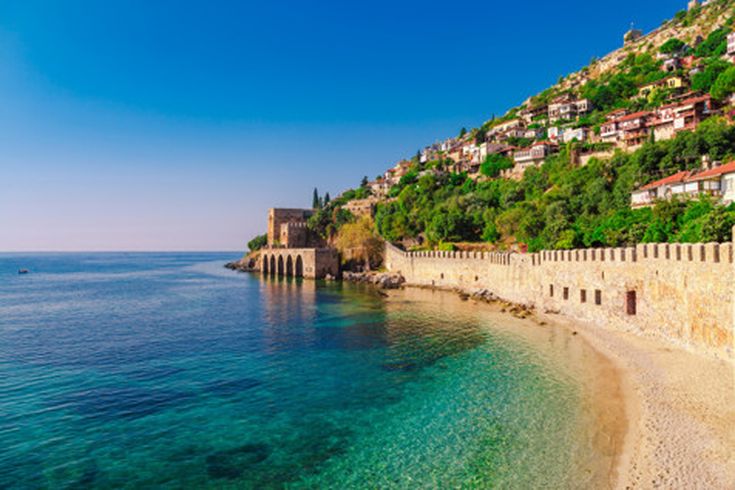 Küstenlandschaft von Alanya mit der historischen Burg, Stadtmauer, klar blauem Meer und Hängen mit traditionellen Häusern