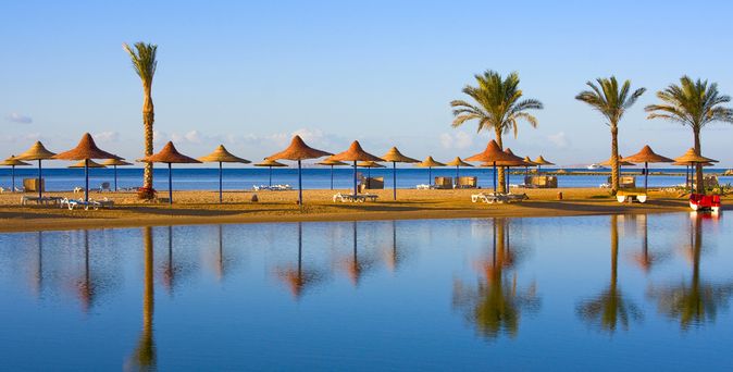 Strand mit Palmen und Sonnenschirmen aus Stroh am ruhigen Meer, Spiegelung im Wasser