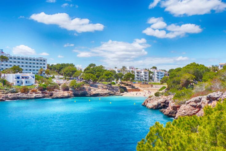 Bucht von Cala d’Or auf Mallorca mit klarem Wasser, Felsen, Pinien und weißen Ferienhäusern am Ufer