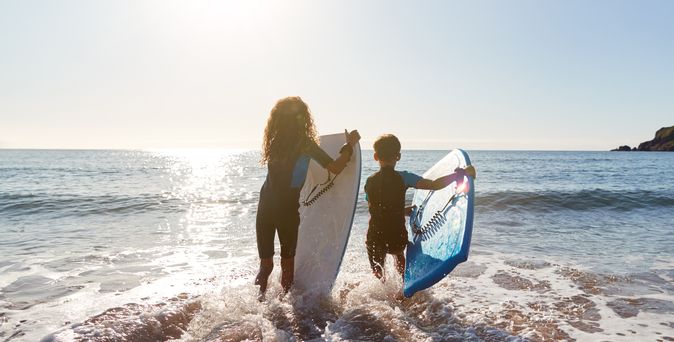 Zwei Kinder mit Surfboards laufen ins Meer, bereit zum Wellenreiten im Sonnenlicht