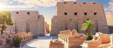 Reihe von steinernen Skulpturen entlang eines Weges zum Eingang des Karnak-Tempels bei Sonnenuntergang