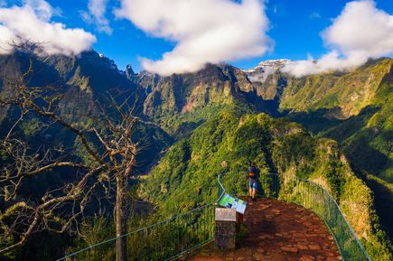 Aussichtsplattform der Vereda dos Balcões auf Madeira mit wandernder Person, tiefgrünen Berglandschaften, zerklüfteten Gipfeln und tiefhängenden Wolken vor blauem Himmel