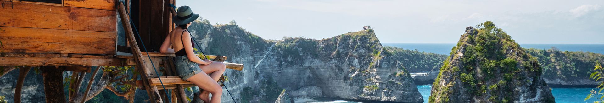 Person sitzt auf einer Holzplattform des Molenteng Tree House auf Nusa Penida bei Bali und blickt über eine türkisfarbene Bucht mit steilen Felsklippen und weißen Sandstränden