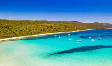 Sakarun Strand auf der Insel Dugi Otok in Kroatien mit flachem, türkisfarbenem Wasser, weißen Booten in der Bucht und grüner Küstenlandschaft