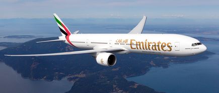 Eine Emirates Boeing 777-300 fliegt über eine weitläufige Insel- und Meereslandschaft, aufgenommen aus der Luft in einer seitlichen Perspektive