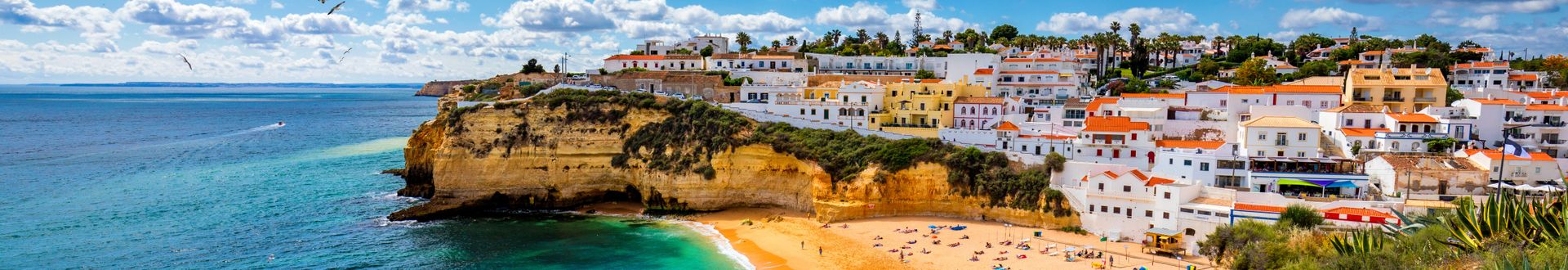 Panoramablick auf den Strand von Carvoeiro an der Algarve mit goldenen Kalksteinfelsen, türkisfarbenem Atlantik, Badegästen, weißen Häusern auf den Klippen und Möwen über der Küste