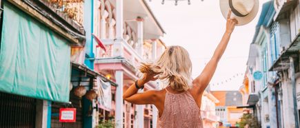 Frau läuft durch die bunte Altstadt von Phuket und hält einen Hut in die Höhe, umgeben von historischen Gebäuden und dekorativen Lichterketten