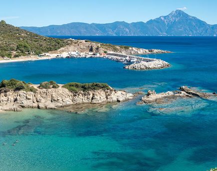 Bucht mit klarem blauem Wasser, felsiger Küste und bewaldeten Hügeln in Chalkidiki, Griechenland