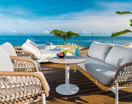 Moderne Rooftop‑Terrasse des Atlantic El Tope mit gemütlichen Lounge‑Sofas, hellen Liegen und Blick auf das Meer, ergänzt durch tropische Pflanzen und einen Tisch mit farbenfrohen Cocktails