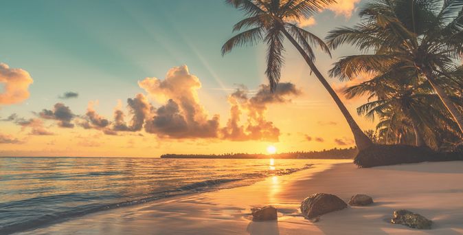 Sonnenuntergang über einem tropischen Strand mit Palmen und ruhigem Meer