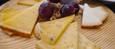 Mehrere Scheiben Käse mit Trauben und Nüssen auf einem Holzbrett angerichtet
