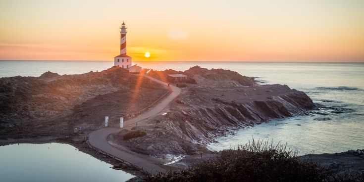 Leuchtturm Cap de Favàritx auf Menorca, umgeben von Felsen, mit untergehender Sonne über dem Meer