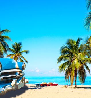 Blauer Oldtimer-Pkw vorne links am Sandstrand mit Palmen und Meer im Hintergrund