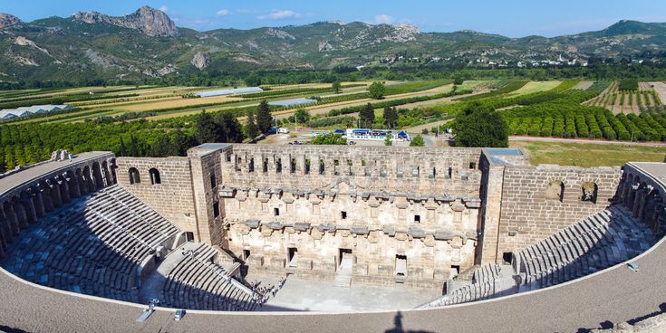 Gut erhaltenes römisches Amphitheater von Aspendos mit halbrunden Sitzreihen, eindrucksvoller Bühnenwand und Blick auf die umliegende Landschaft.