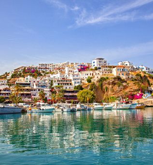 Hafen mit Booten vor einem Hügel mit weißen Häusern und blühenden Pflanzen auf Kreta
