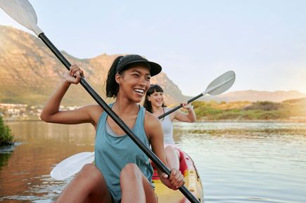 Zwei Personen im Kanu paddeln auf einem ruhigen Gewässer, umgeben von Bergen und Vegetation
