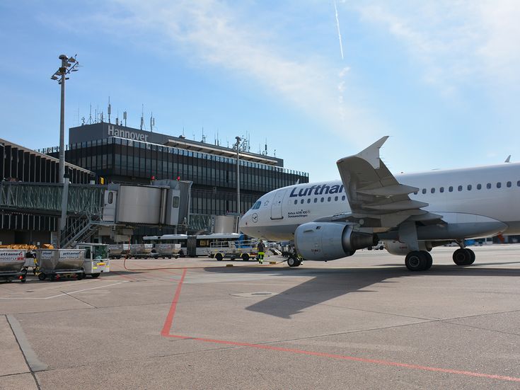 Flugzeug auf dem Vorfeld des Flughafens Hannover neben einer Fluggastbrücke, umgeben von Bodenfahrzeugen und Terminalgebäude.