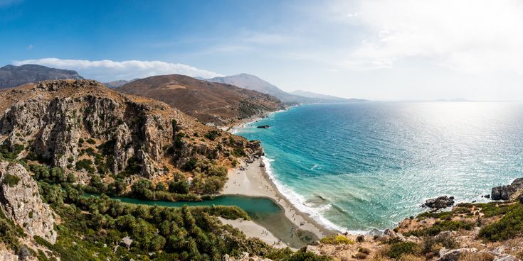 Panoramablick auf den Strand von Preveli auf Kreta, mit klarem Wasser, Sandstrand und umgebenden Bergen.