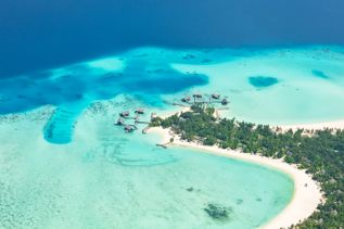 Luftaufnahme eines kleinen tropischen Inselresorts im Raa-Atoll der Malediven mit Sandstrand, grüner Vegetation und über dem Wasser gebauten Bungalows