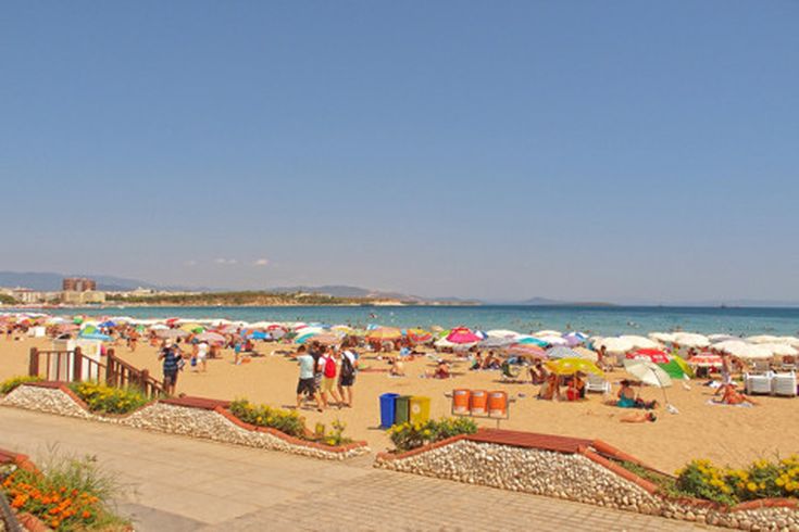 Belebter Altinkum-Strand in Didim, Türkei, mit vielen bunten Sonnenschirmen, Urlaubern am Sandstrand und Blick auf das blaue Meer unter klarem Himmel