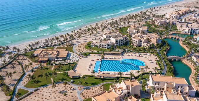 Luftaufnahme des Salalah Rotana Resort im Oman mit großem Pool, palmengesäumter Gartenanlage, Lagunen und direkter Lage an einem weitläufigen Sandstrand am Arabischen Meer