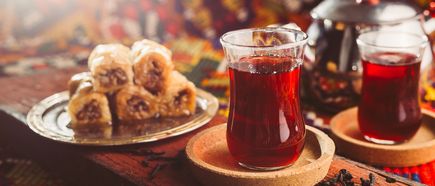 Glas türkischer Schwarztee neben Baklava auf Tablett, warmes Licht und orientalisches Ambiente