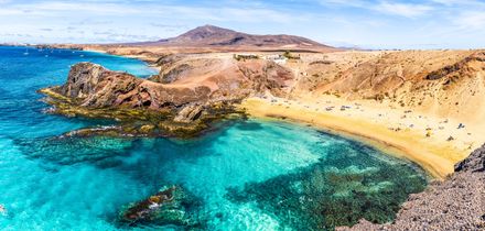 Bucht mit klarem türkisfarbenem Wasser, Sandstrand und felsiger Küste auf den Kanarischen Inseln unter blauem Himmel