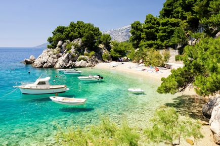 Idyllische Badebucht an der Makarska Riviera in Mitteldalmatien, Kroatien, mit türkisblauem Wasser, kleinen Booten, Kiesstrand und Pinien vor felsiger Küste