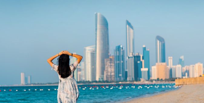 Frau steht am Strand und blickt auf die Skyline von Abu Dhabi