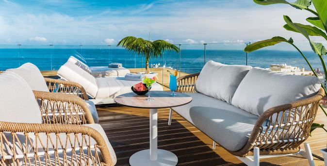 Moderne Rooftop‑Terrasse des Atlantic El Tope mit gemütlichen Lounge‑Sofas, hellen Liegen und Blick auf das Meer, ergänzt durch tropische Pflanzen und einen Tisch mit farbenfrohen Cocktails