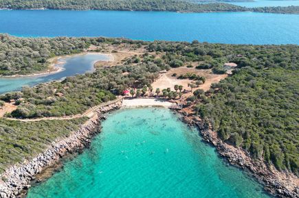 Luftaufnahme des Kleopatra Beach auf Sedir Island in der Türkei, mit türkisfarbenem Wasser, hellem Sandstrand und dichter grüner Vegetation rund um die Bucht