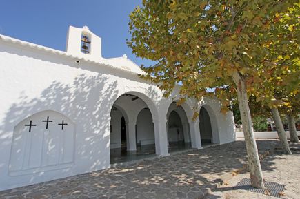 Weiße Kirche Sant Carles de Peralta auf Ibiza mit Arkaden und schattenspendenden Bäumen davor
