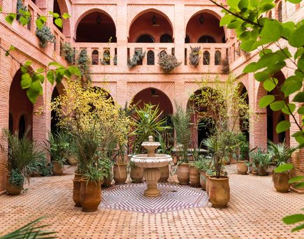 Ruhiger, marokkanischer Innenhof mit Arkaden, vielen Pflanzen und einem zentralen Brunnen.